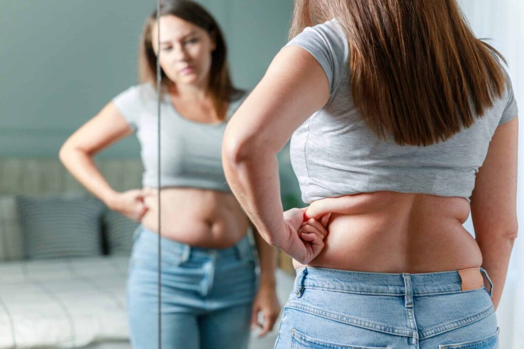 Hasi zsír eltüntetése – nő a tükörben vizsgálja a hasát
