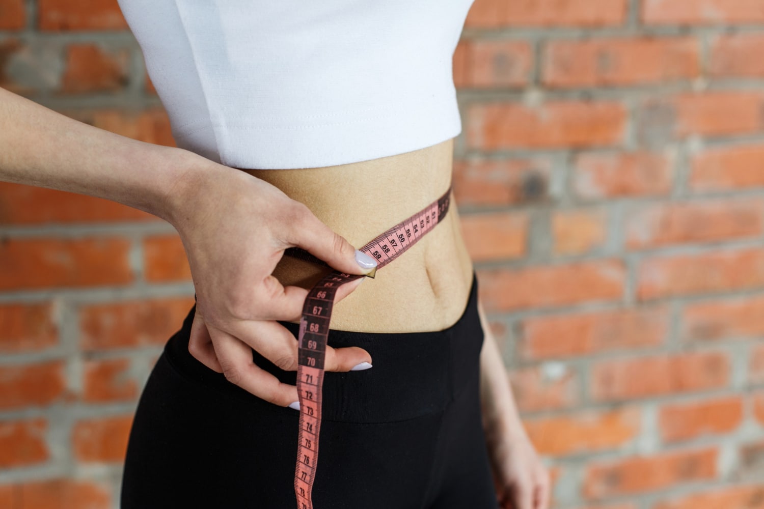 Nő fehér felsőben méri a derekát centivel, a fogyókúrás injekciók hatásának eredményét mutatva.